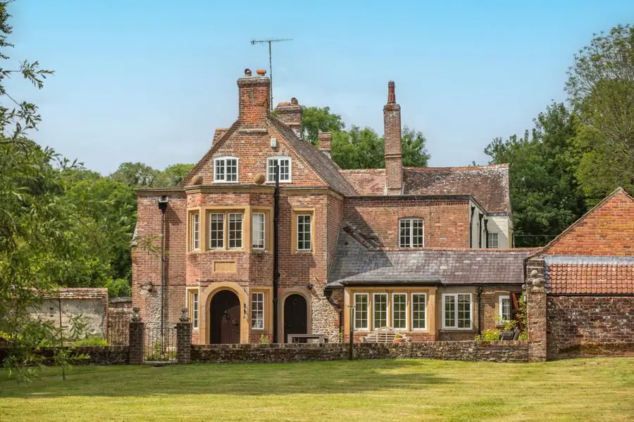 A red-brick country house behind a walled lawn